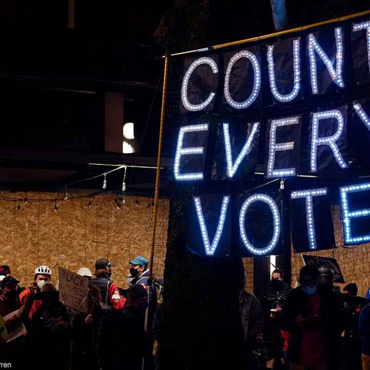 Demonstrators carrying a banner with the text "Count Every Vote" spelled out in LED bulbs.