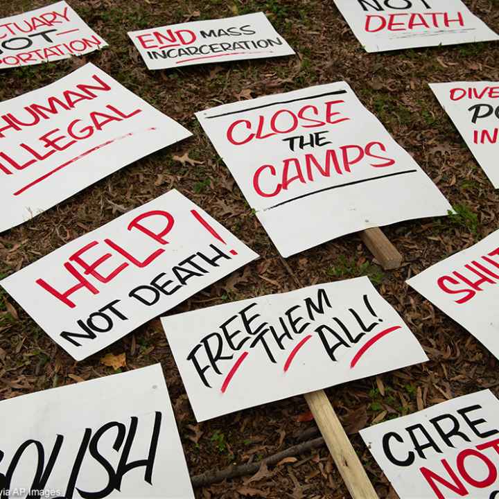 Several signs with calls to end mass incarceration and advocate for the rights of immigrants lying in the grass.