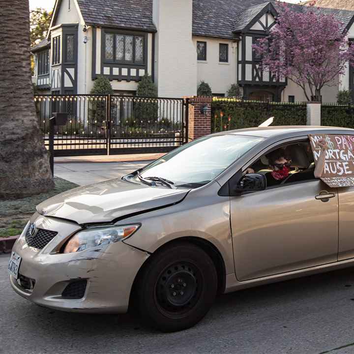 A protestor drives by L.A. Mayor Eric Garcetti's mansion with a sign in favor of extended rent and mortgage protections.