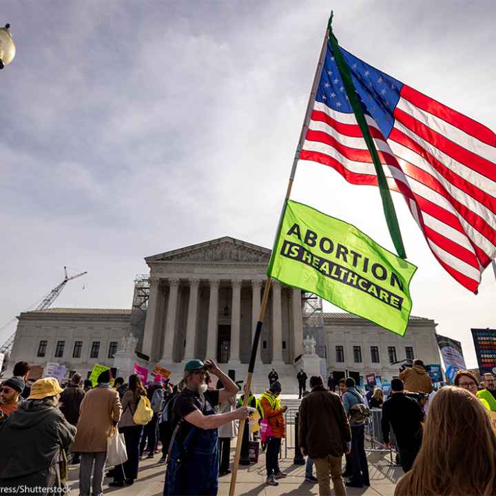 A demonstrator holds up a pole with an American flag on top and another flag reading "ABORTION IS HEALTHCARE" below it as others protest the proposed limited use of mifepristone outside the U.S. Supreme Court on the 26th of March 2024.