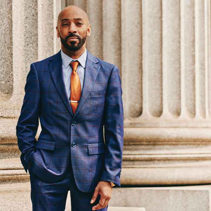 Daudi Justin standing in front of a marble column with his left hand in his pant pocket.