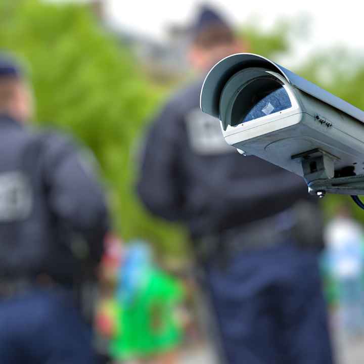 A security CCTV camera or surveillance system with police officers in the blurry background.