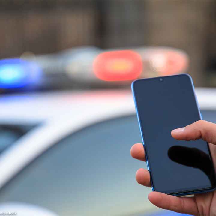 Hand holding phone with police car lights shining in the background.