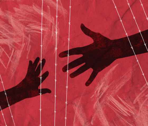 Two hands reaching for one another behind a wired fence